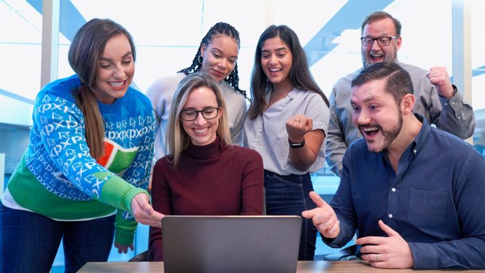 men and women sitting and standing while staring at laptop